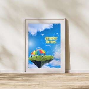 Pode incluir: Uma impressão emoldurada com um fundo de céu azul e nuvens brancas. A impressão apresenta um grupo de pessoas brincando com um paraquedas colorido em uma ilha flutuante. O texto "simpler times." está escrito em letras amarelas no céu.