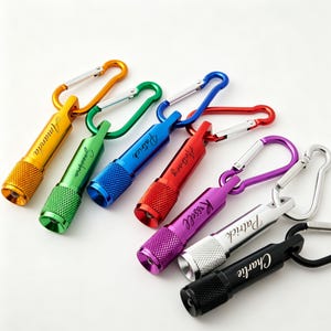 Puede incluir: Una colección de siete linternas cilíndricas de metal, cada una unida a un mosquetón a juego. Las linternas son de color amarillo, verde, azul, rojo, morado, plateado y negro, con nombres grabados en el lateral de cada unidad.