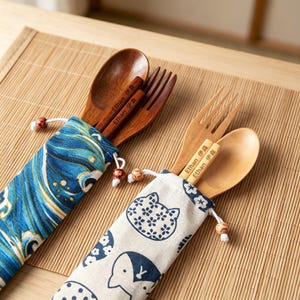 May include: Two sets of wooden cutlery, each containing a spoon, a fork, and a pair of chopsticks, stored in fabric pouches. One pouch features a blue wave pattern, while the other has a white cat print. The chopsticks are engraved with "Ethan 伊森".