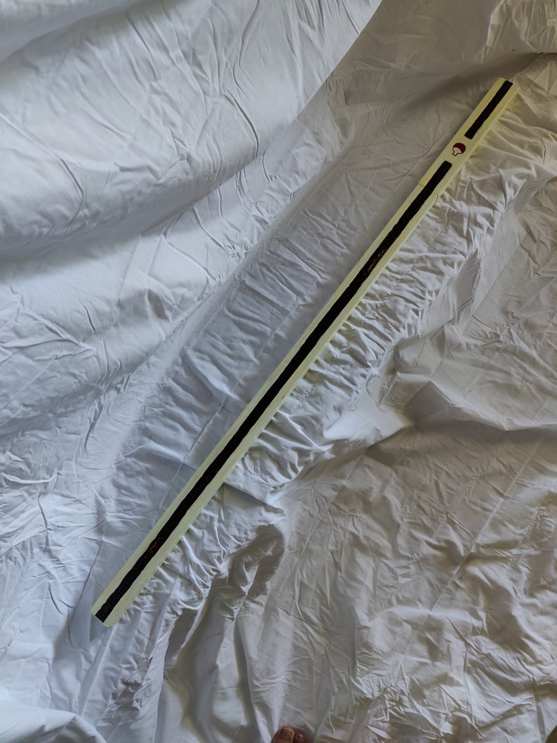 K&ouml;nnte beinhalten: Ein langer, wei&szlig;er Holzstab mit einem schwarzen Streifen, der in der Mitte verl&auml;uft. Der Stab hat einen roten Kreis oben.