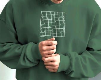 May include: A dark green sweatshirt featuring a white Sudoku puzzle graphic on the front. The word "sudoku" is printed below the puzzle. The sweatshirt has long sleeves and a crew neck.