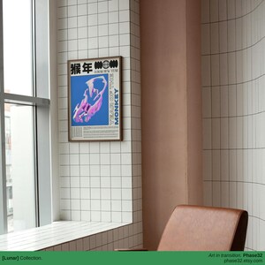 Poster hung on a clean, curved wall beside a modern chair, highlighting its bold typography and surreal monkey form.