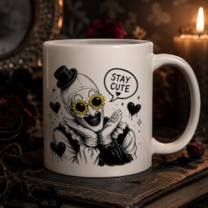 May include: A white ceramic mug featuring a black and white illustration of a clown wearing a top hat and sunflower-shaped glasses. The clown has hands pressed against its cheeks, and a speech bubble above reads STAY CUTE with a small heart.