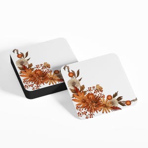 May include: Two white square coasters featuring a floral design in shades of orange, brown, and white. The flowers are arranged in a corner of the coaster.