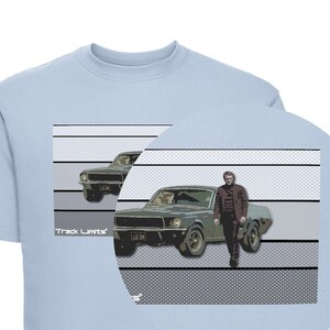 Puede incluir: Sudadera azul claro con un gráfico de un coche verde clásico y una persona con una chaqueta marrón. El diseño incluye el texto "Track Limits" y una matrícula. El fondo tiene un patrón gris y blanco.