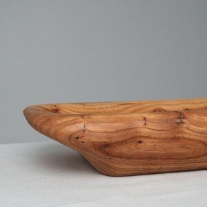 May include: A large, wooden serving bowl with a natural wood finish. The bowl is made from a single piece of wood and has a unique, organic shape.