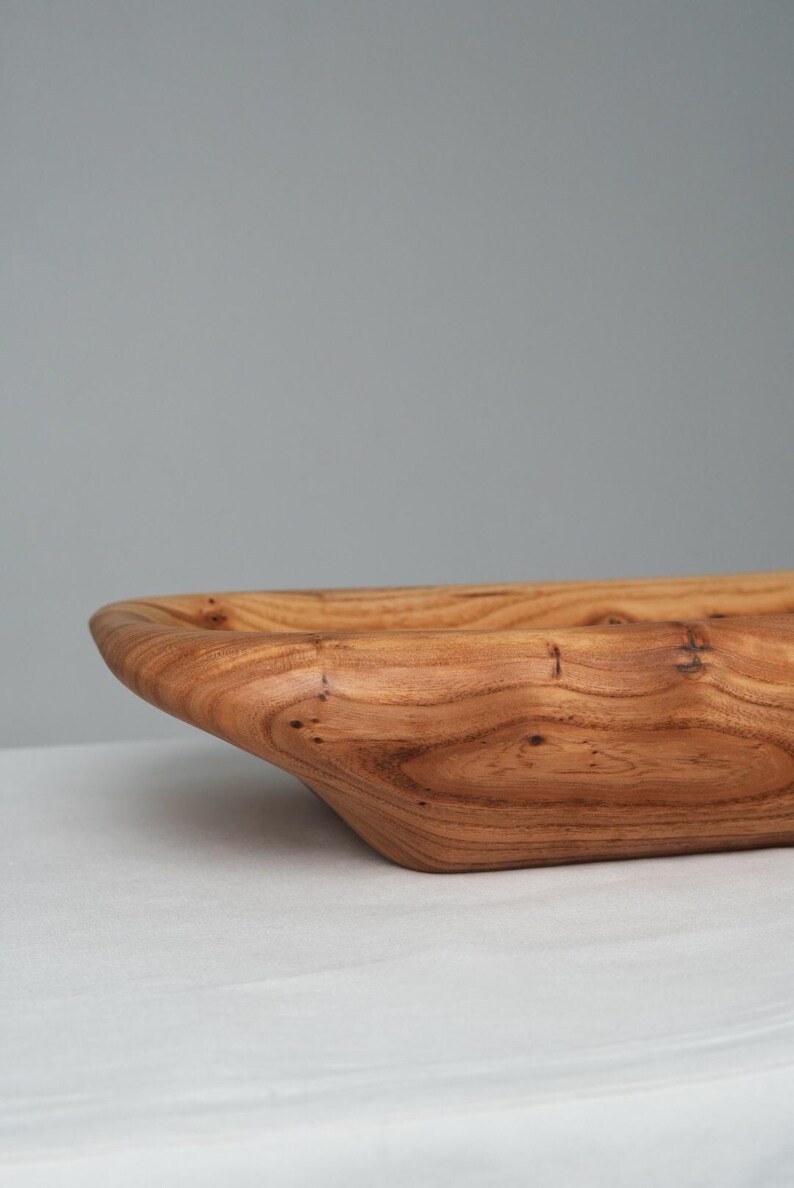 May include: A large, wooden serving bowl with a natural wood finish. The bowl is made from a single piece of wood and has a unique, organic shape.
