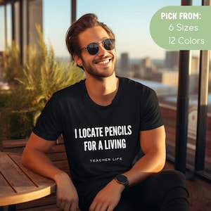 May include: A black t-shirt with white text that reads "I locate pencils for a living" and "Teacher Life".