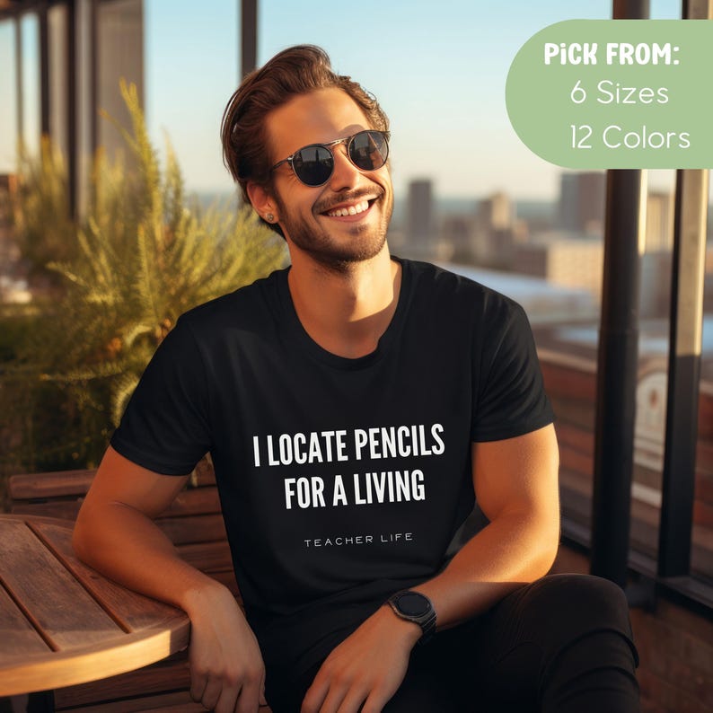 May include: A black t-shirt with white text that reads "I locate pencils for a living" and "Teacher Life".