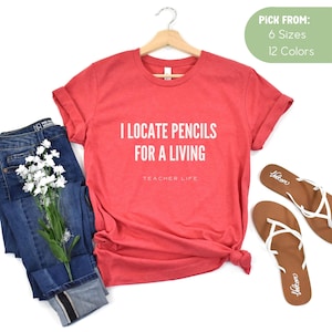 May include: Red short-sleeved t-shirt with the text "I locate pencils for a living" and "Teacher Life" in white.