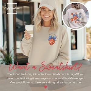 May include: Beige sweatshirt with a patriotic strawberry design. The strawberry has a blue bow and is filled with white stars. The text "freedom, dancing, party" is above the strawberry. The image also shows the text "Want a Sweatshirt?"