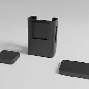 Puede incluir: Una caja de plástico negro con una abertura rectangular en la parte delantera. La caja está abierta y tiene dos tapas de plástico negro separadas.