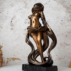 May include: A bronze-colored statue of a woman with long flowing hair and a helmet. The statue has a black base and is set against a neutral background. The figure's form is stylized, with a focus on flowing lines and curves.