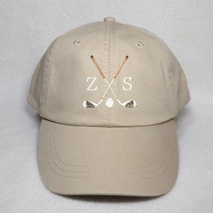 Peut inclure: Une casquette de baseball beige avec un motif brodé blanc de deux clubs de golf croisés et les lettres "ZS".