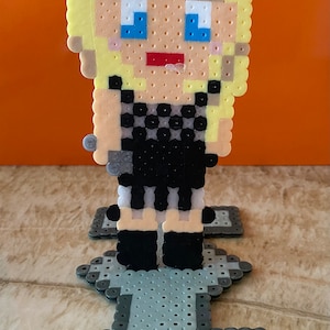 May include: A pixel art figure of a person with blonde hair wearing a black and white checkered dress and black shoes. The figure is standing on a gray platform.