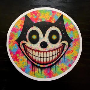 May include: A round sticker featuring a black cat face with a wide, unsettling grin. The cat's eyes are yellow, and the background is a colorful splatter of paint in various hues. The sticker has a white border.