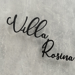 Puede incluir: Un letrero de metal negro con las palabras "Villa Rosina" en una fuente cursiva.