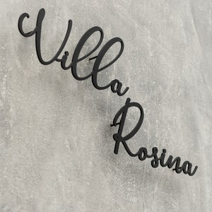 Puede incluir: Letrero de metal negro con las palabras "Villa Rosina" en una fuente cursiva.