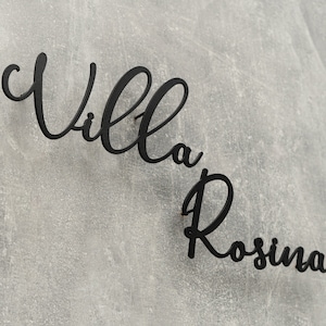 Puede incluir: Letrero de metal negro con las palabras "Villa Rosina" en escritura cursiva.