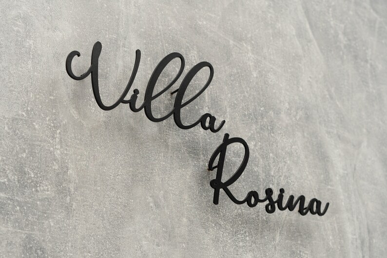 Puede incluir: Letrero de metal negro con las palabras "Villa Rosina" en escritura cursiva.