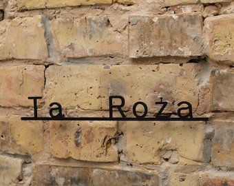 Puede incluir: Un letrero de metal negro con las palabras "Ta Roza" en una pared de ladrillo.