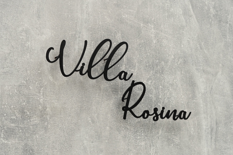 Puede incluir: Letrero de metal negro con las palabras "Villa Rosina" en una fuente cursiva.