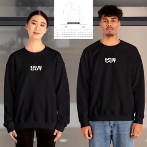 Puede incluir: Sudadera negra de cuello redondo con el texto blanco "ICE OUT" en el pecho. La sudadera la llevan dos personas. Una tabla de tallas es visible en el fondo. La sudadera es de estilo unisex.