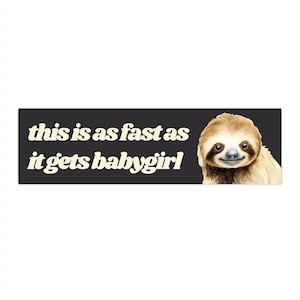 May include: A rectangular sticker with a black background and white text that reads "this is as fast as it gets babygirl." A watercolour illustration of a sloth is on the right side of the sticker.