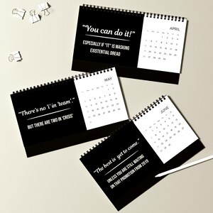 May include: Black and white desk calendars with spiral binding. Each calendar features a month view and a humorous quote in white text. One calendar reads "You can do it!" and another says "There's no 'i' in 'team'."