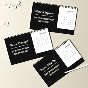 May include: A collection of black desk calendars with white text and dates. Each calendar features a different motivational quote, including "Make it happen," "Be the Change," and "Never Give Up." The calendars are spiral-bound.