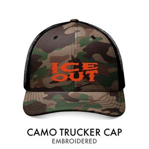 Puede incluir: Gorra de camionero camuflada con el texto "ICE OUT" bordado en naranja. La gorra presenta un patr&oacute;n de camuflaje en tonos verdes, marrones y negros, con una parte trasera de malla negra. Es una gorra de estilo camionero cl&aacute;sico.