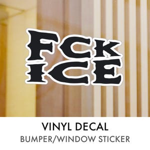May include: Black vinyl decal with the words "FCK ICE" in a bold, stylized font. The decal is a bumper or window sticker, with the words stacked vertically. The background is a light wood grain.