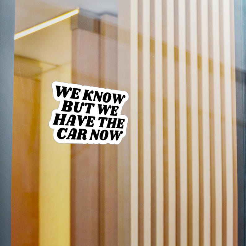 Op de afbeelding: Witte sticker met zwarte tekst die "We know but we have the car now" zegt.