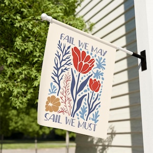 May include: A cream-coloured garden flag with a floral design and the text "FAIL WE MAY SAIL WE MUST." The design features red tulips, blue and brown floral elements, and blue accents. The flag is mounted on a white pole.