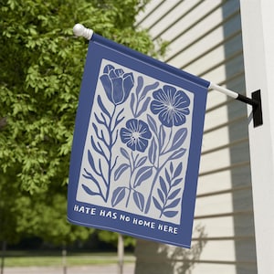 May include: A blue and white garden flag with a floral design. The flag has a rectangular shape with a dark blue border and a white background. The design includes stylized flowers and leaves in shades of blue. The text "HATE HAS NO HOME HERE" is at the bottom.