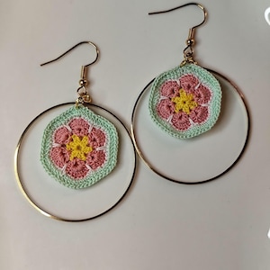 Peut inclure: Une paire de boucles d'oreilles créoles dorées avec des accents de fleurs crochetées. Les fleurs sont roses, vertes et jaunes.