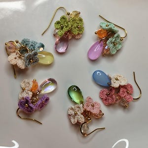 May include: Five pairs of crocheted flower earrings with dangling teardrop-shaped beads in various colors, including pink, green, blue, and yellow.