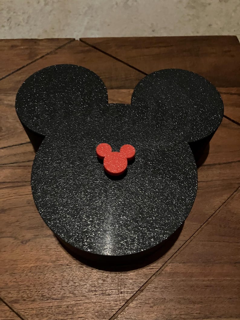 K&ouml;nnte beinhalten: Schwarze Mickey-Maus-Kopf-f&ouml;rmige Box mit einem roten Mickey-Maus-Kopf auf der Vorderseite.