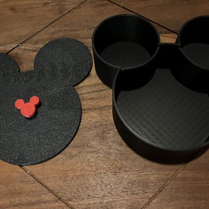 K&ouml;nnte beinhalten: Schwarzer Mickey-Maus-f&ouml;rmiger Aufbewahrungsbeh&auml;lter mit drei F&auml;chern. Der Deckel ist ein separates Teil mit einem roten Mickey-Maus-Kopf in der Mitte.