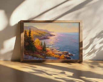 May include: A framed landscape painting depicting a coastal scene with a rocky shoreline, evergreen trees, and autumn foliage in shades of orange and yellow. The ocean water reflects the soft light of a sunset, with distant hills visible under a pale sky.