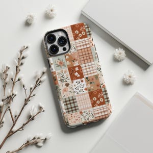 Puede incluir: Una funda de teléfono con un diseño de patchwork que presenta patrones florales y de cuadros en tonos marrones, beige y blancos.