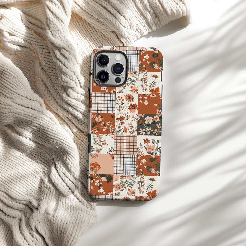 May include: A white phone case with a patchwork design featuring floral and geometric patterns in shades of brown, orange, and cream.