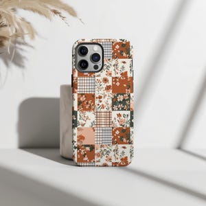 May include: A white phone case with a patchwork design featuring orange, brown, and green floral patterns. The case has a cutout for the phone's camera.