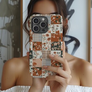 May include: A white phone case with a patchwork design featuring brown, green, and pink floral patterns. The case has a camera lens cutout.