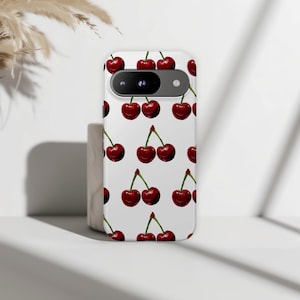 May include: A white phone case featuring a repeating pattern of watercolor-style cherries. The cherries are a deep red color with green stems. The phone case has a camera cutout and is sitting on a white surface.