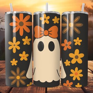 Op de afbeelding: Drie zwarte geïsoleerde bekers met bloemen- en spookontwerpen. Eén beker heeft een spook met een strik, terwijl de andere oranje en gele bloemen hebben. Elke beker heeft een zilveren deksel en een rietje.