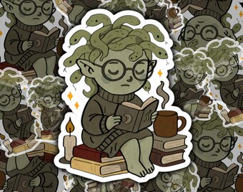 May include: A sticker featuring a cartoon Medusa reading a book while sitting on a stack of books. She wears glasses and a sweater, with snakes for hair. A mug of coffee and a lit candle are also present. The sticker has a white border.