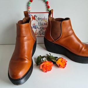 Può includere: Un paio di stivaletti in pelle marrone con una suola platform spessa. Gli stivaletti hanno un design slip-on e una punta leggermente a punta.