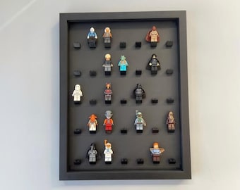 Puede incluir: Un marco de exhibición rectangular negro que contiene catorce pequeñas figuras de plástico dispuestas en cinco filas sobre un fondo gris oscuro. Cada figura está montada sobre un pequeño bloque negro, mostrando diversos atuendos y accesorios.