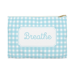 Puede incluir: Una bolsa con cremallera con estampado de cuadros vichy azul claro y blanco con la palabra "Breathe" en una fuente cursiva azul claro. La palabra está dentro de un marco rectangular blanco. La cremallera es dorada.